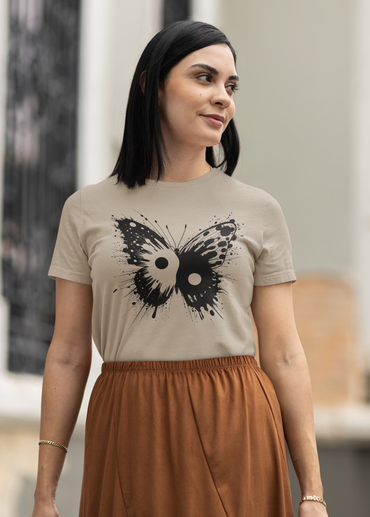 A woman wearing a beige t-shirt with a black butterfly graphic and a rust-brown skirt, standing in front of a softly blurred building background.