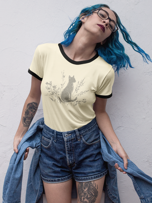 A person with bright blue hair and glasses poses against a white textured wall, wearing a pale yellow ringer T-shirt with a black collar and sleeve trim, a gray cat graphic, blue denim shorts, and holding a blue denim jacket.